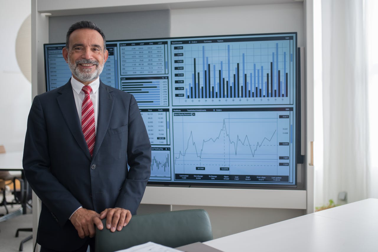 Services-01 Smiling businessman in office analyzing financial graphs on a large screen, demonstrating professional success.